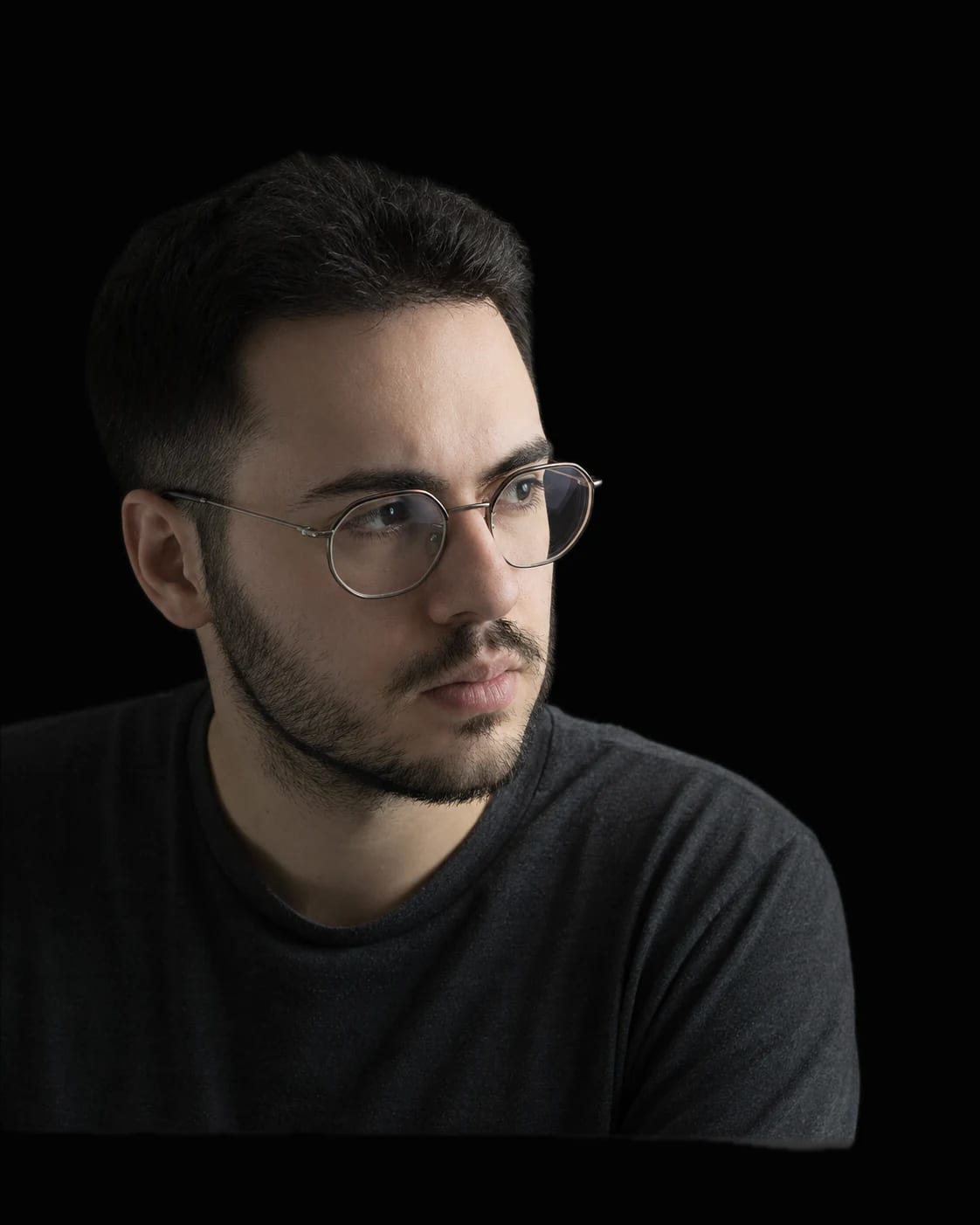 Francesco Romito, ritratto in chiaroscuro su fondo grigio scuro: occhiali, maglia scura, lo sguardo rivolto verso il testo, un accenno di scrivania nel buio in basso.